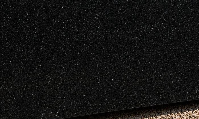 A polished jet-black granite block standing on gravel in the stone yard, reflecting the sky